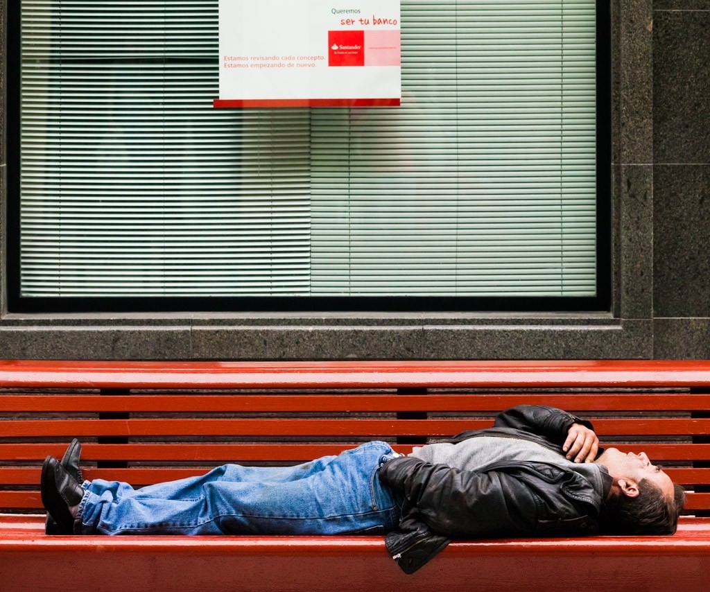 hombre durmiendo en un banco frente al banco Santander